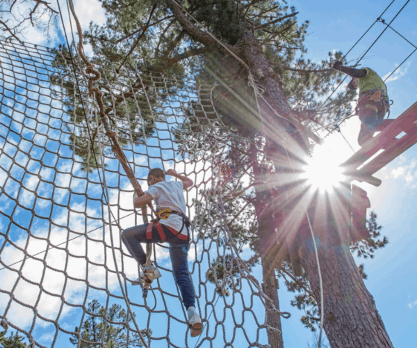 Client climbing on a cargo net during a Treetop adventure experience and instructor offering on-course support